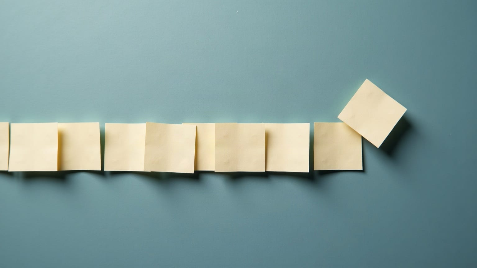 A row of identical paper squares with one lifted out of the line and tilted above it